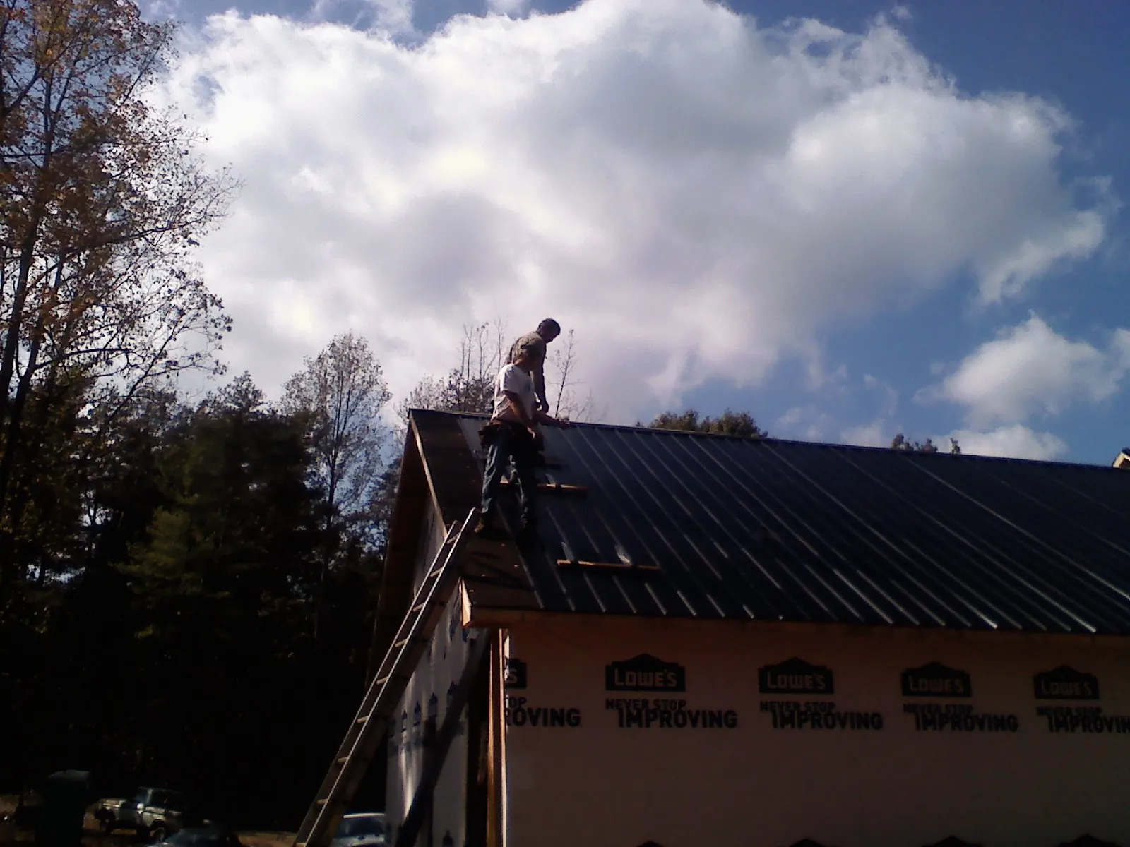 Roofer fastening dark metal panels high against a cloudy sky, from a Roof Inspection job in Indian Trail
