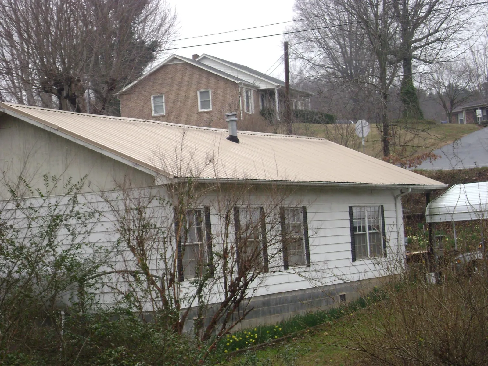 Tan metal roof on a white sided house set into a hillside — Commercial Roofing by Roofing Brothers in Indian Trail